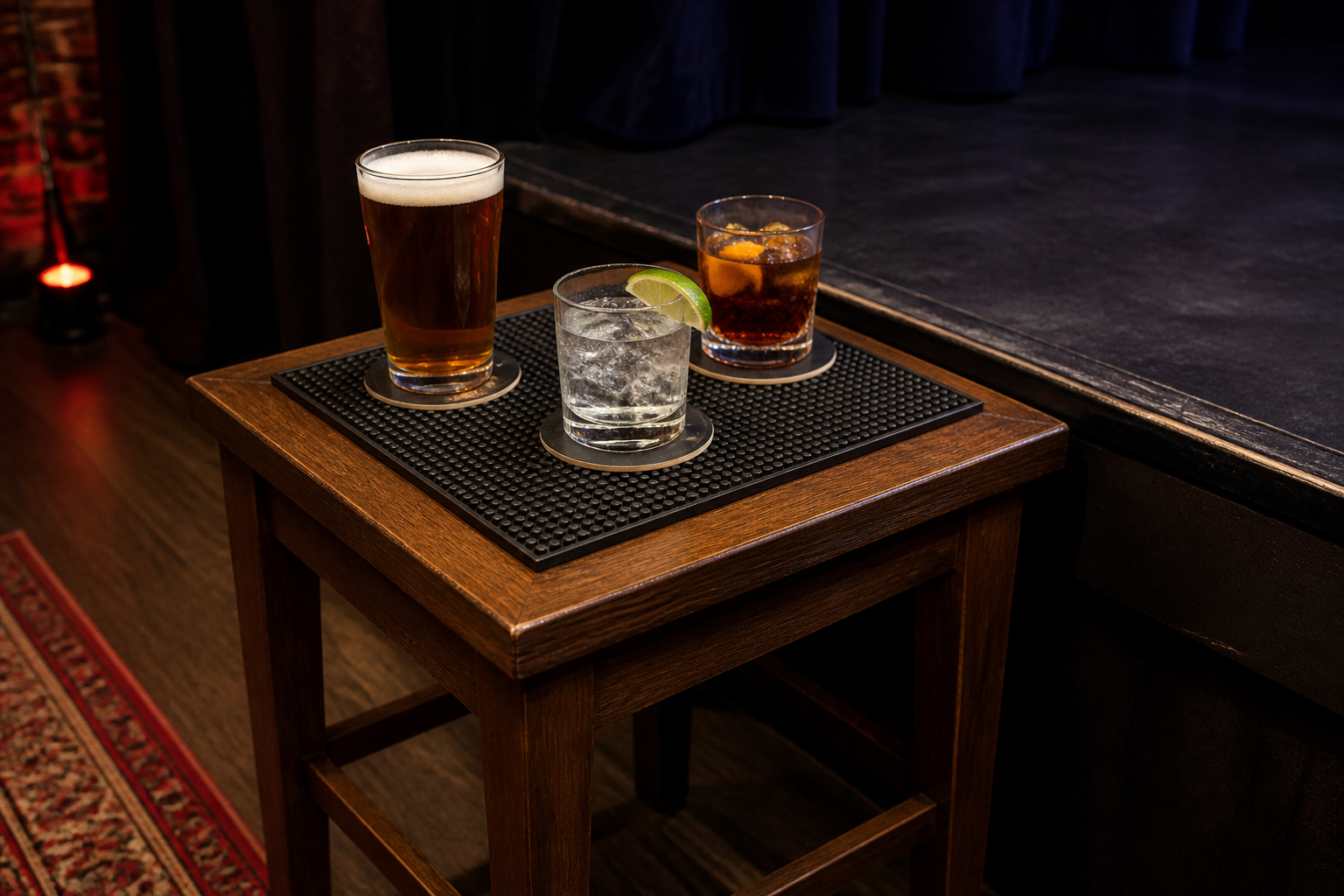 Small wooden table beside a stage with drinks on coasters and a non-slip mat